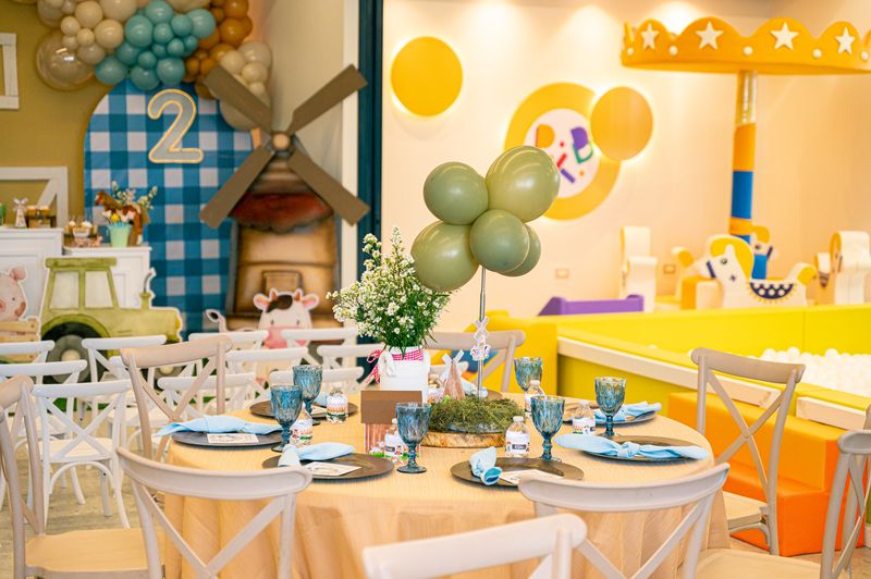 Mesa redonda decorada con globos verdes, el molino y el número 2 de la fiesta de granja